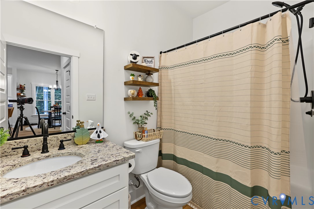 Bathroom featuring a stone-surface vanity with an integrated undermount sink, dark-finish faucet, wall-spanning mirror, three tiered floating wood shelves, and a tub-shower combination with a dark-finish rainfall showerhead
