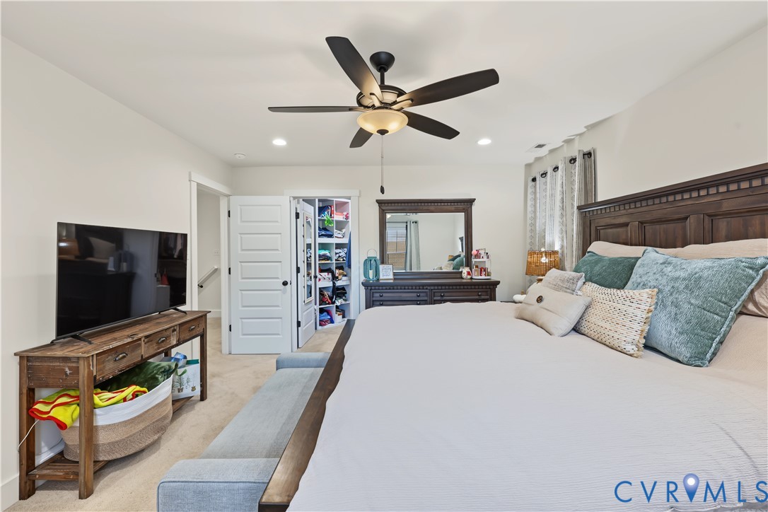 Bedroom interior featuring neutral wall paint, carpeting, recessed lighting, a five-blade ceiling fan with integrated light fixture, and a walk-in closet with built-in shelving