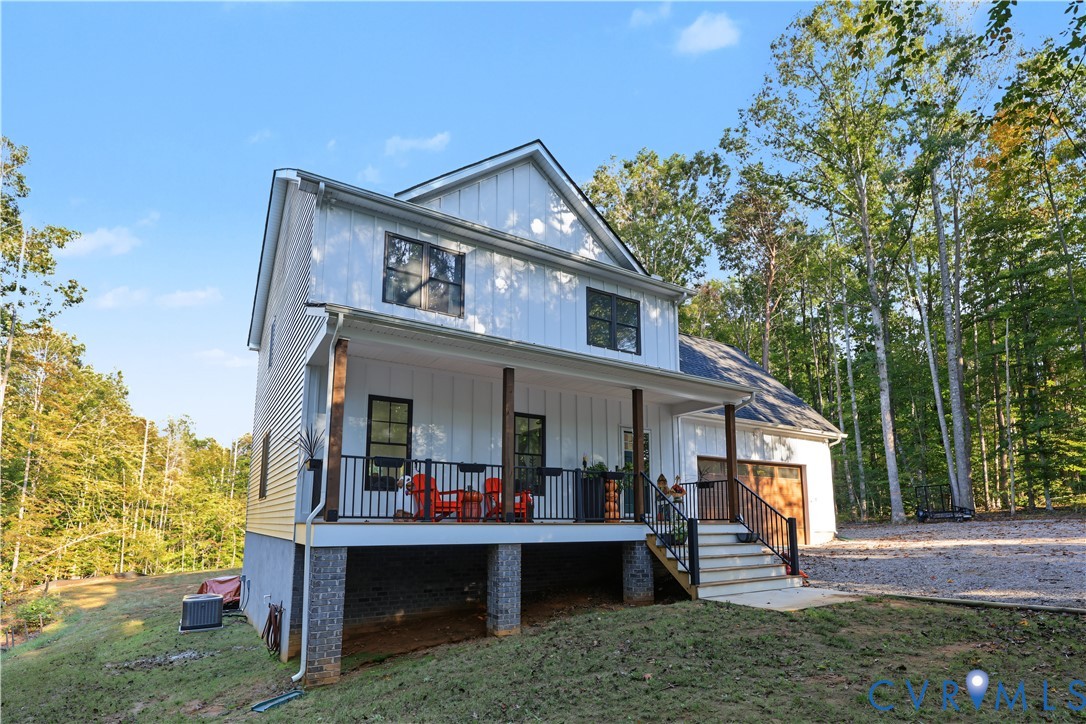 Two-story residence featuring white board-and-batten siding, a raised covered porch with dark metal railings, wood-wrapped support pillars, and a multi-car garage