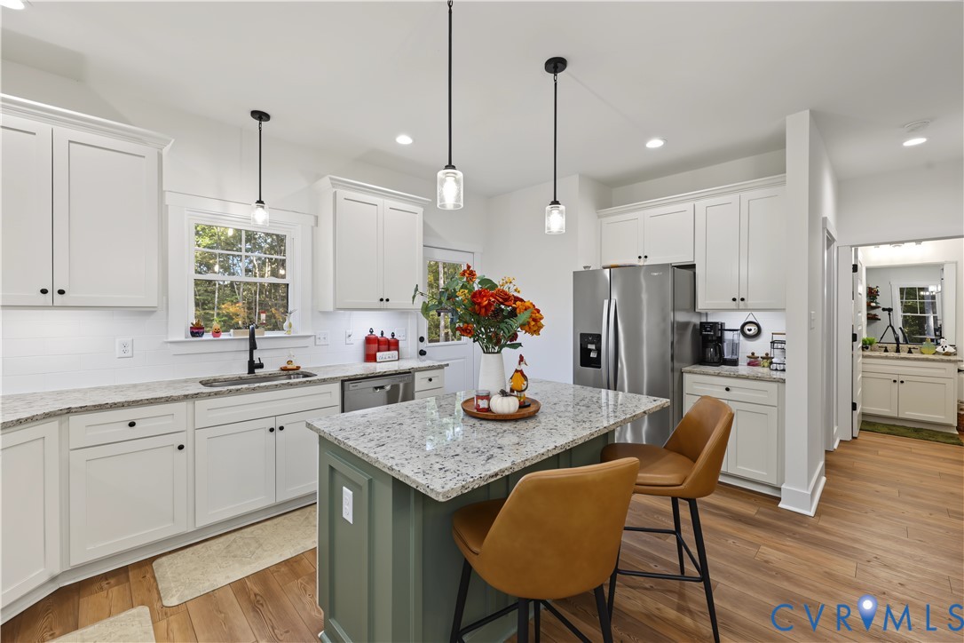 Kitchen featuring white shaker cabinetry, speckled stone countertops, a contrasting green center island, wood-finish flooring, and pendant lighting