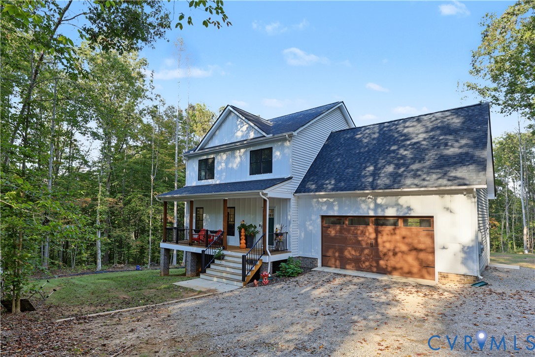 Two-story home with white vertical and horizontal siding, covered front porch, wood-finished garage door, and stone foundation elements