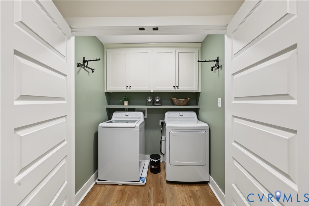 Laundry area featuring white shaker-style wall cabinetry, built-in shelving, wood-finish flooring, and dual-door entry