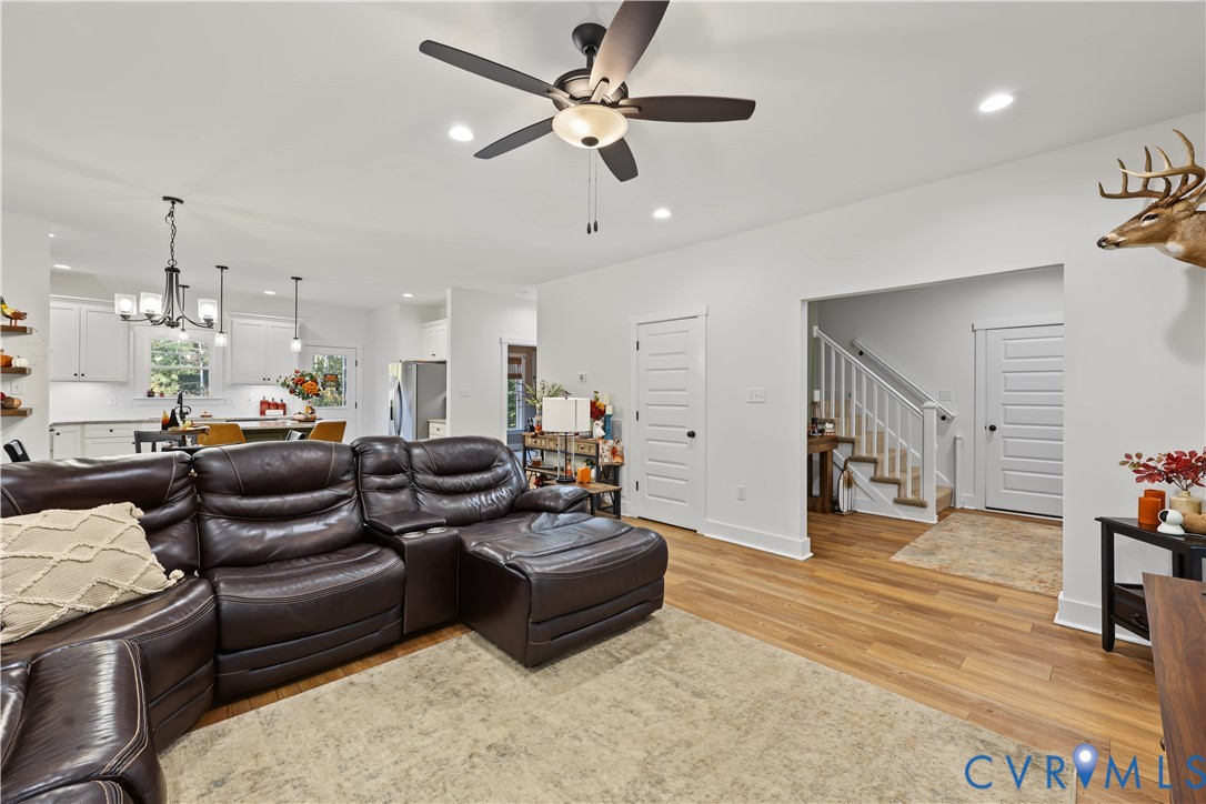 Open-concept interior featuring wood-finish flooring, a multi-blade ceiling fan, recessed lighting, and a white staircase with a wooden handrail
