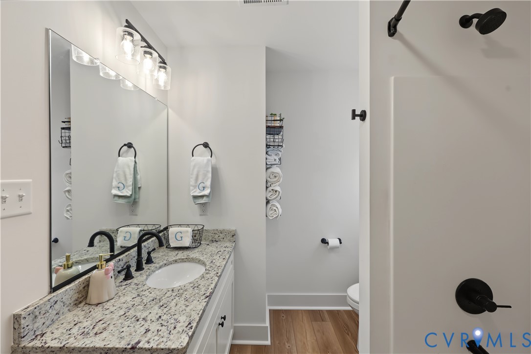 Vanity featuring a stone countertop with an integrated oval sink, matte black faucet, wall-mounted lighting, and wood-finish flooring