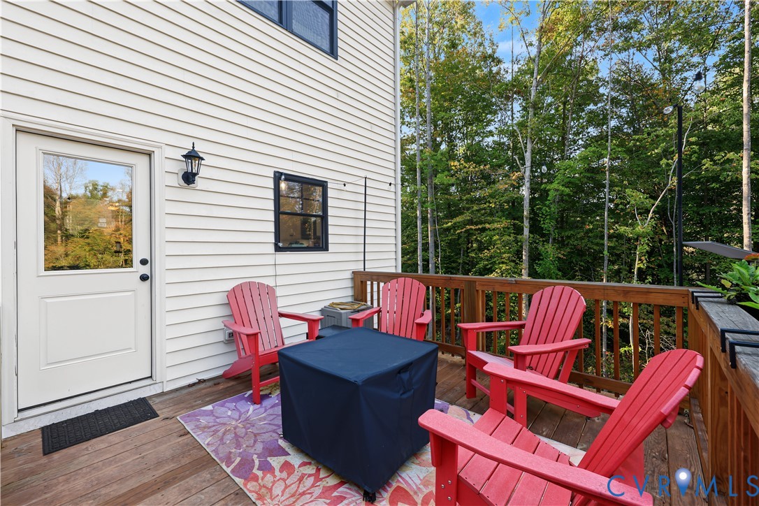 Exterior wood deck featuring a railing and attached wall-mounted light fixture, with light-colored horizontal siding and a glass-paneled door