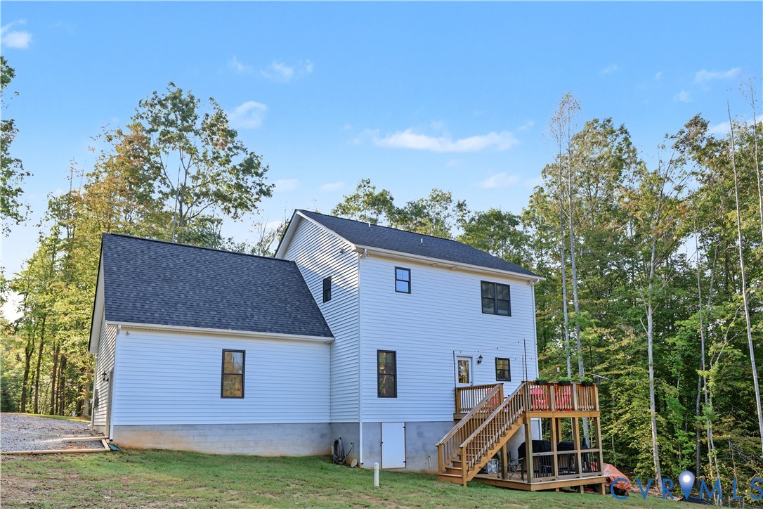 Two-story home with white horizontal siding, asphalt shingle roofing, elevated wood deck with stairs, and exterior basement access door