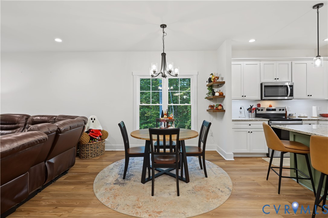 Kitchen featuring white shaker-style cabinetry, a kitchen island with stone countertops, wood-finish flooring, recessed lighting, and a multi-arm chandelier