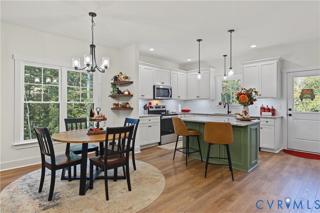 Kitchen featuring white cabinetry, center island with an olive green base and stone countertop, stainless steel appliances, wood-finish flooring, and pendant lighting