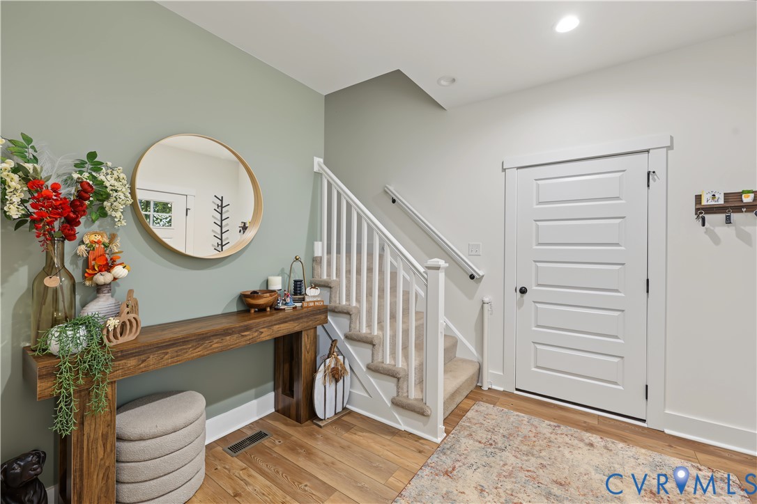 Entryway featuring a five-panel shaker-style door, wood-finish flooring, and a staircase with white balusters and carpeted treads, accented by a painted sage feature wall