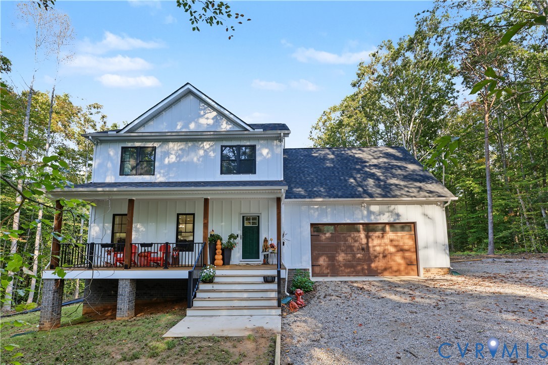 Two-story residence featuring white board-and-batten siding, a covered front porch with dark metal railings, a stone-accented foundation, and a double-car garage with a wood-finish door