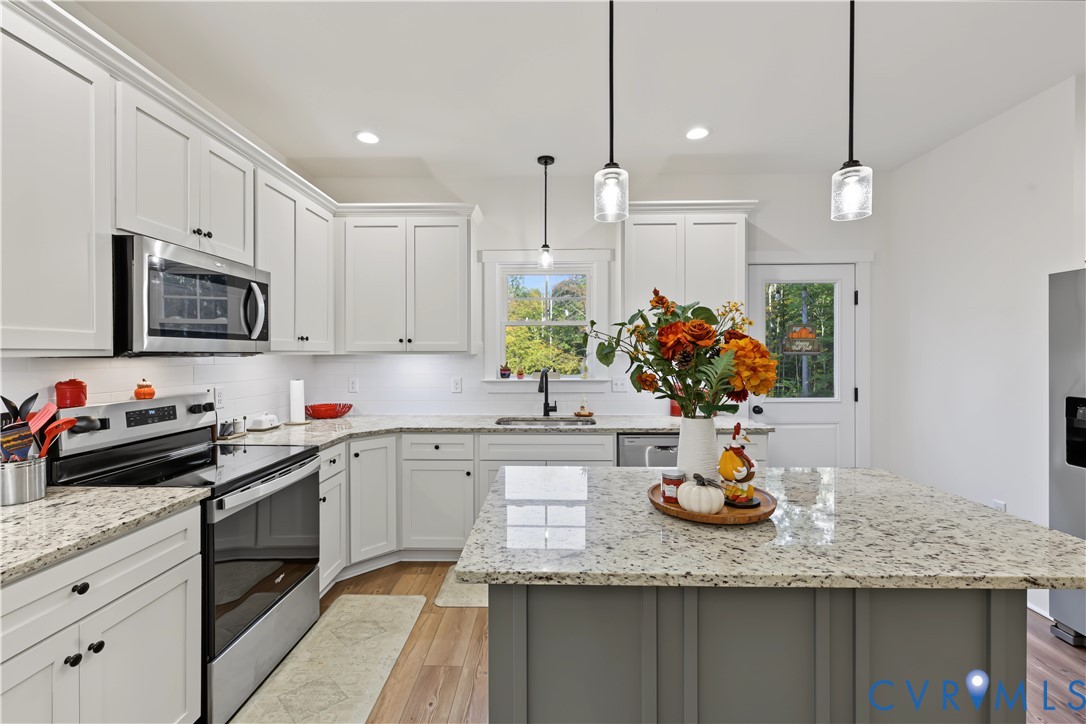 Kitchen featuring white shaker-style cabinetry, stone countertops, a central island with a contrasting base, stainless steel appliances, and wood-finish flooring
