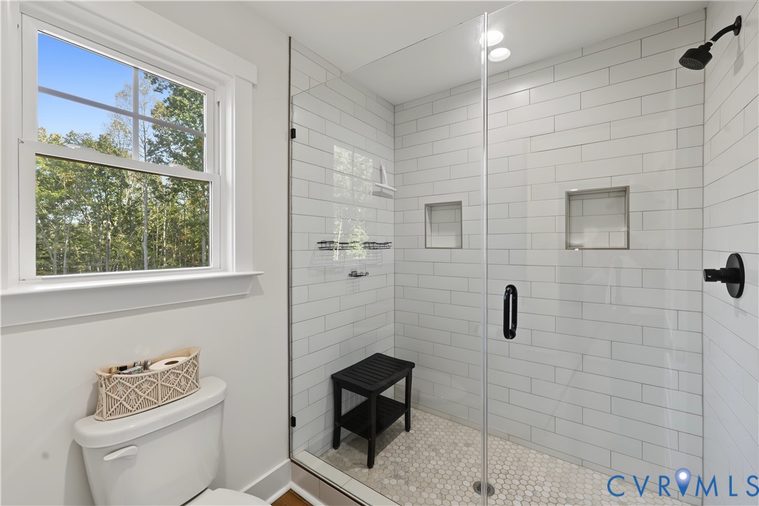 Walk-in shower featuring white subway tile walls, a frameless glass door, dual built-in wall niches, and a penny-round tile floor