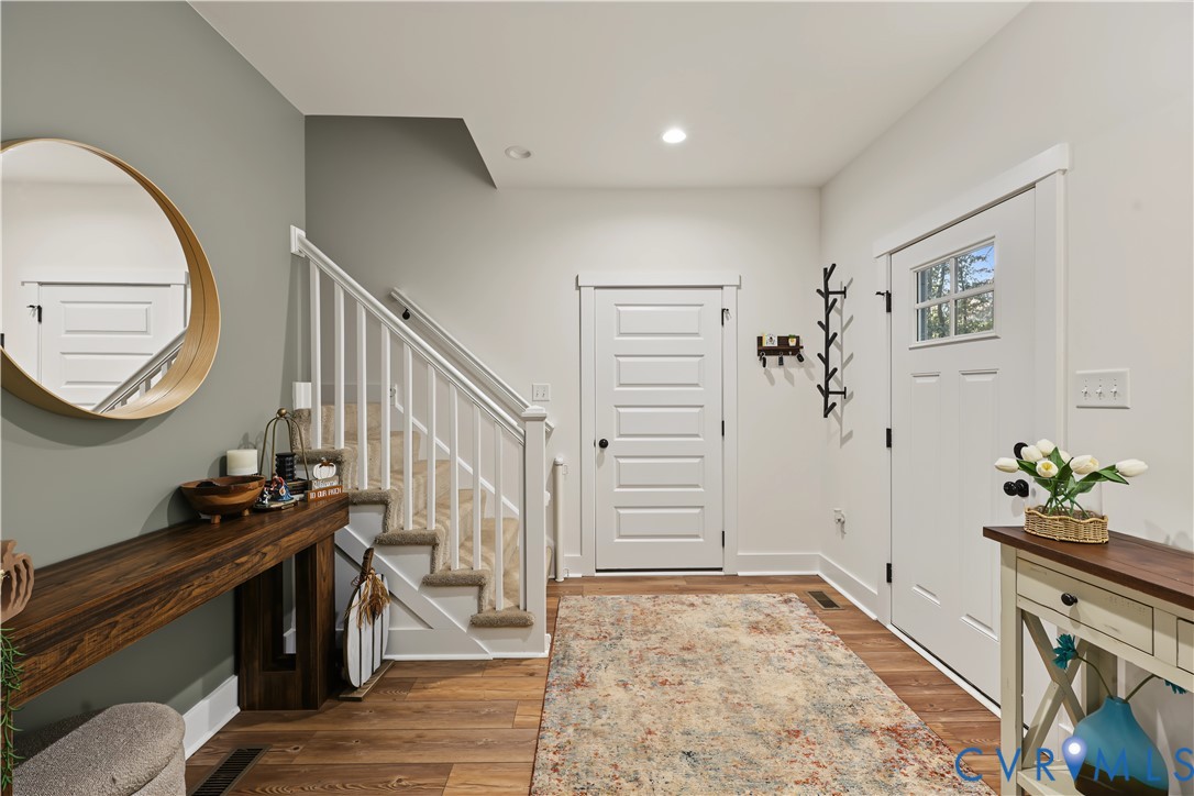 Entryway featuring wood-finish flooring, a white five-panel door with a glass lite, and a staircase with a white balustrade