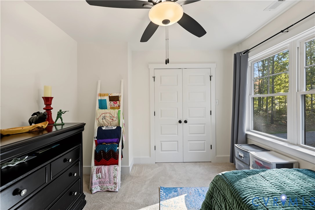 Interior room featuring wall-to-wall carpeting, double doors with paneled detailing, a multi-blade ceiling fan with integrated lighting, and dual windows
