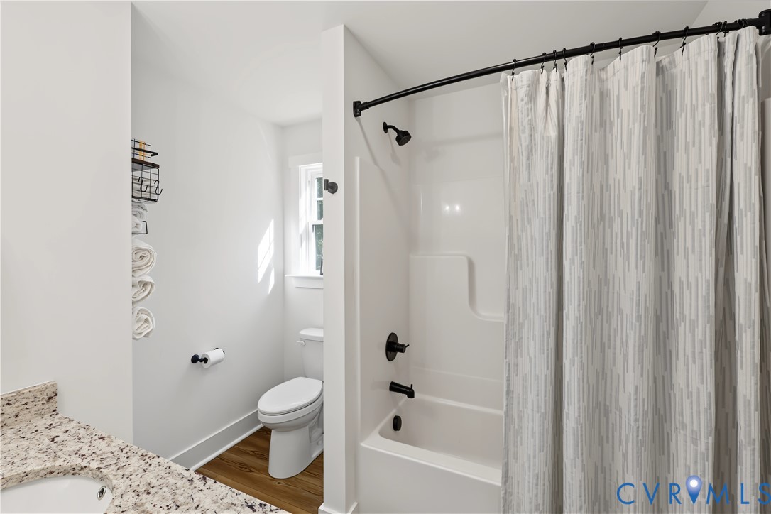 Bathroom featuring a composite tub surround with matte black plumbing fixtures, wood-finish flooring, and a stone-surface vanity countertop