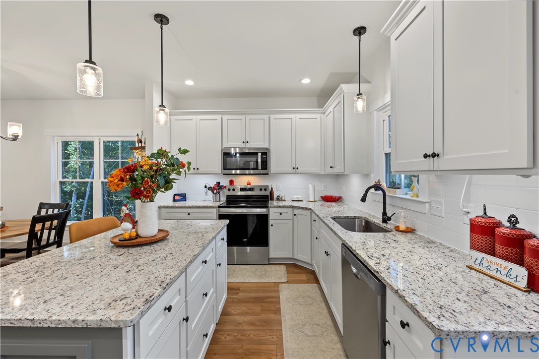 Kitchen featuring white cabinetry, stone-surface countertops, central island, stainless steel appliances, and wood-finish flooring