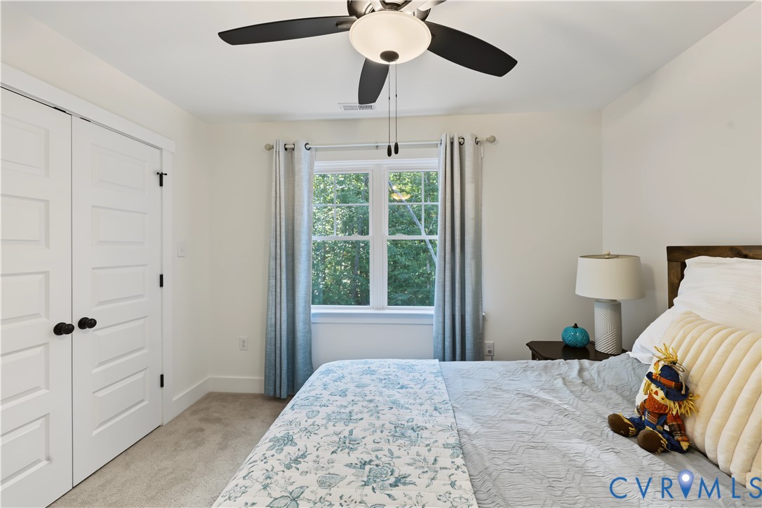 Double-door closet with panel detailing, ceiling fan with integrated lighting, window with multi-pane grilles, and neutral-toned wall-to-wall carpeting