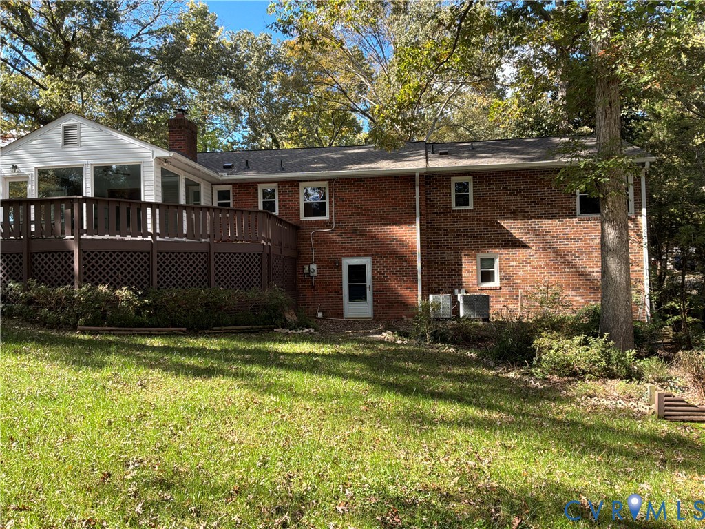 Multi-level exterior featuring a brick facade, elevated wood deck with lattice skirting, shingled roof, and rear-facing windows