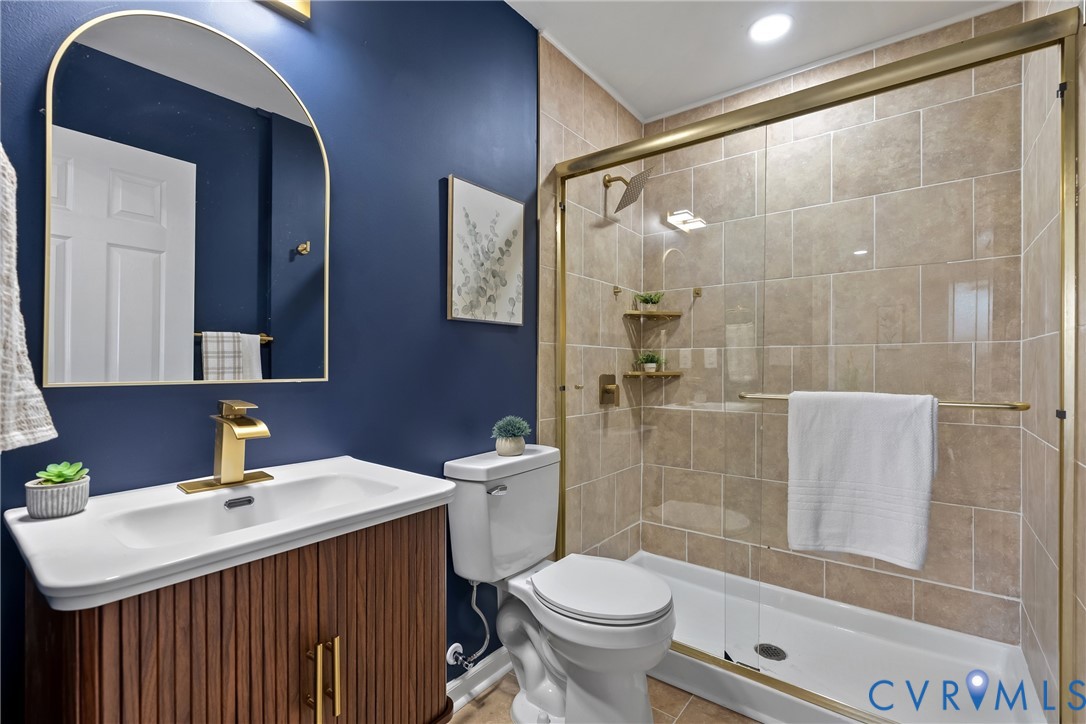 Bathroom featuring a ribbed wood-finish vanity, arched gold-framed wall mirror, gold-toned faucet, and a walk-in shower with tiled surround and gold-toned frame