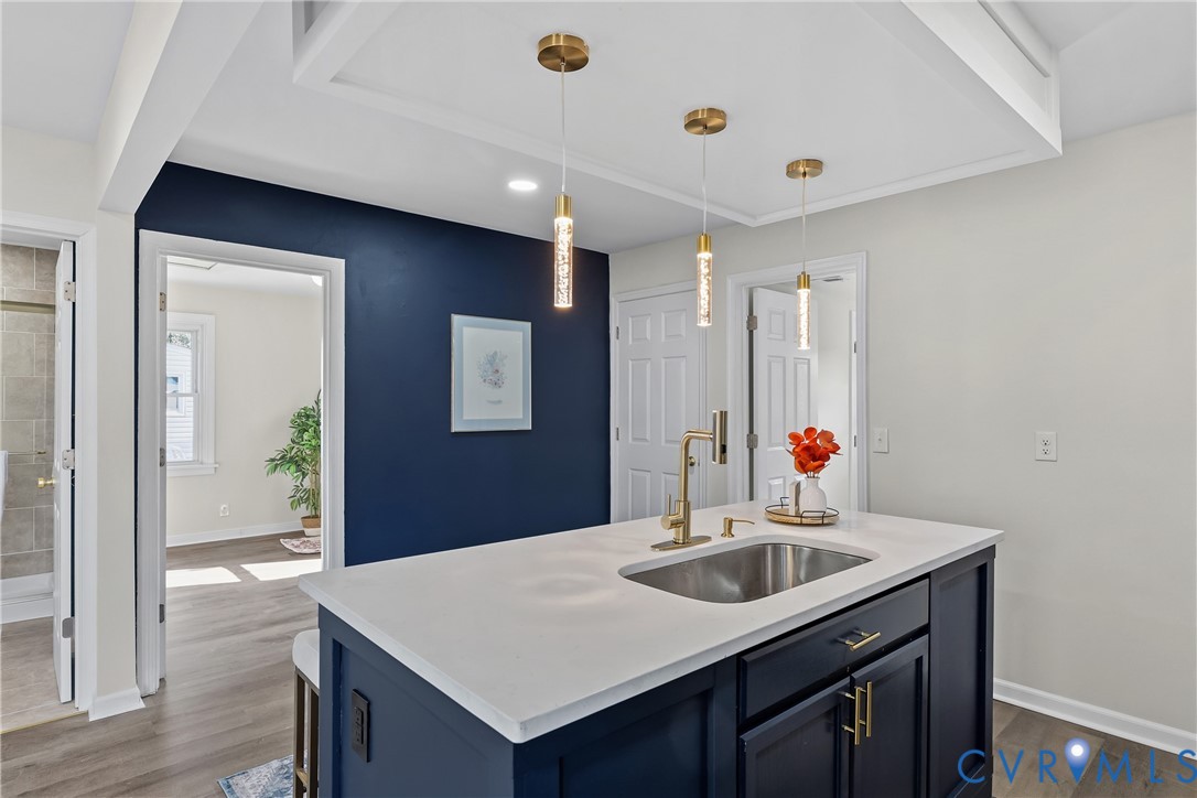 Kitchen island featuring a white countertop, undermount stainless steel sink, brass-finish faucet, and navy blue cabinetry with metallic hardware, accented by three suspended cylindrical pendant lights