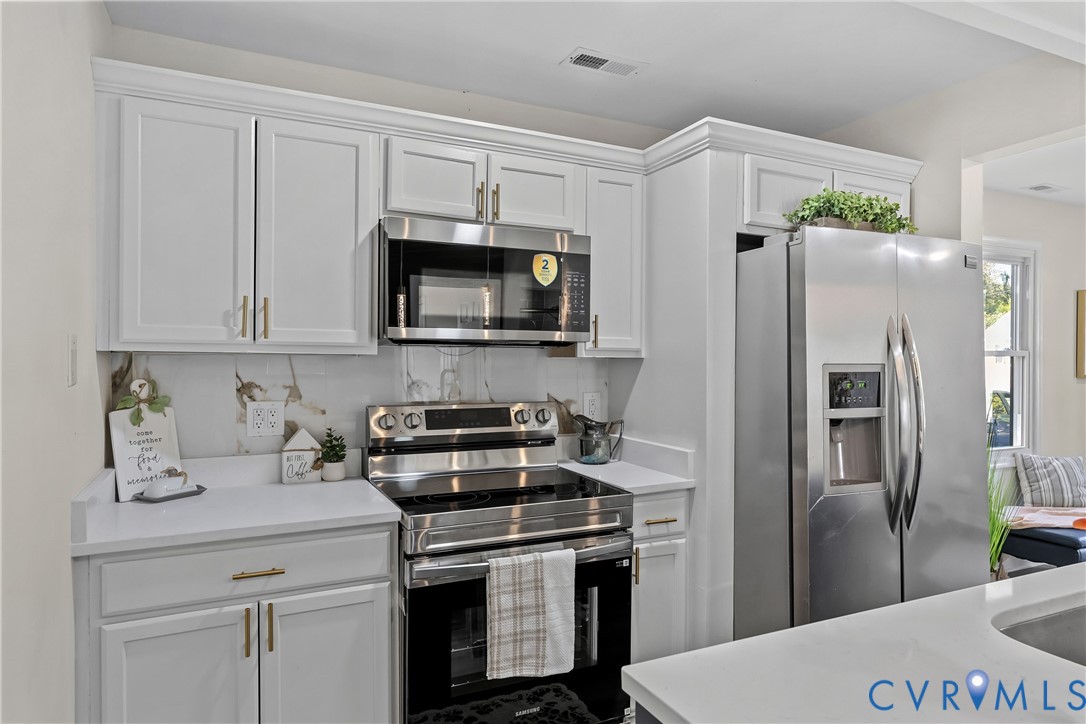 Kitchen featuring white shaker-style cabinetry with brass-finish pulls, solid surface countertops, stainless steel appliances, and a built-in microwave