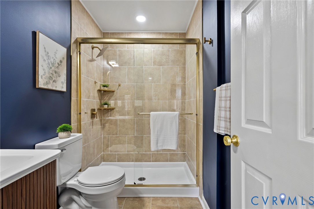 Full bathroom featuring a shower stall with gold-finish frame and fixtures, neutral stone-finish tile surround, built-in shelving, and dark-toned walls