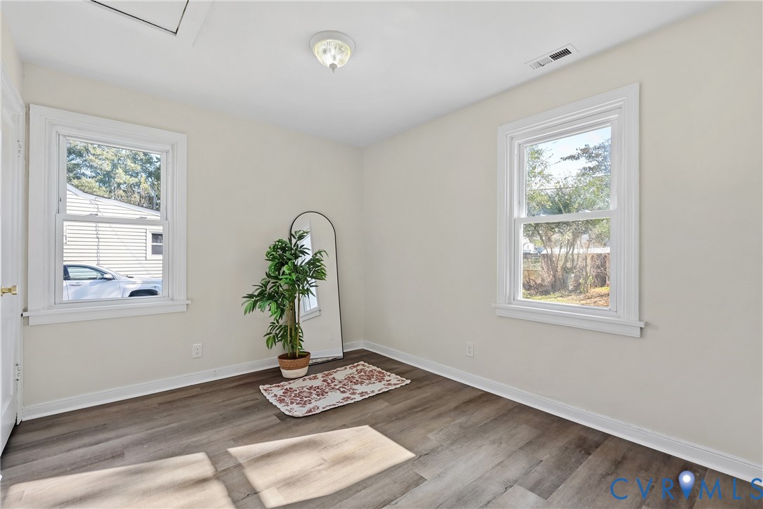 Interior space featuring neutral wall paint, wood-finish flooring, two double-hung windows with white casing, and a flush-mount ceiling light fixture