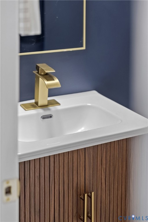 Fluted wood-finish vanity with a white integrated sink, polished gold-tone faucet, matching cabinet hardware, and gold-trimmed mirror