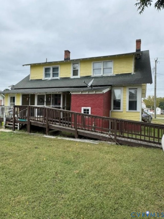 Two-story exterior featuring yellow horizontal siding, a red brick base, two brick chimneys, and an attached wood-railing ramp