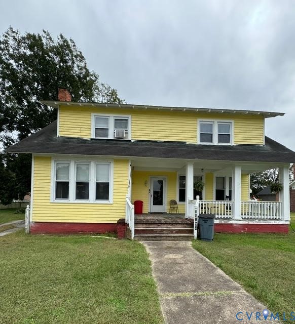 Two-story exterior featuring yellow lap siding, a wrap-around front porch with square columns, a dark shingled roof, and a concrete walkway
