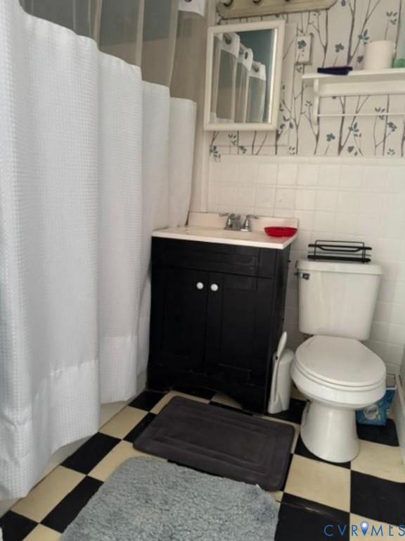 Black vanity with a white countertop, wall-mounted rectangular mirror, built-in shelving, checkered flooring, and white square-tile wall surround