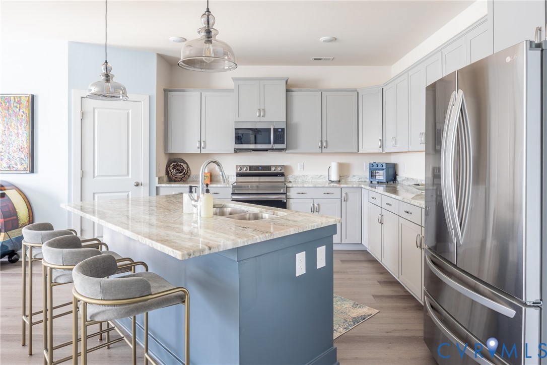 Kitchen featuring light gray cabinetry, a blue-painted center island with a stone-surface countertop, stainless steel appliances, and wood-finish flooring