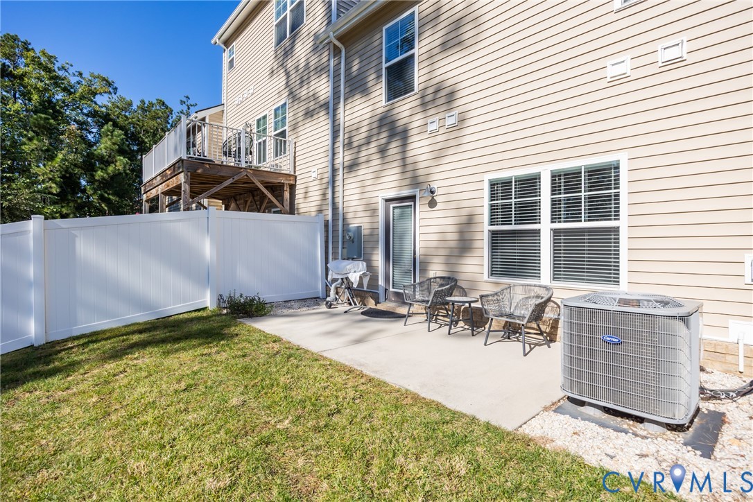 Vinyl-sided exterior featuring an elevated deck with a white railing, a concrete ground-level patio, and white privacy fencing