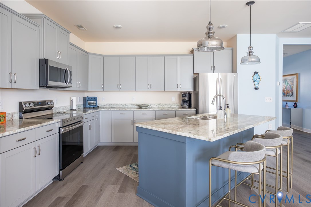 Kitchen featuring gray cabinetry, stone-finish countertops, stainless steel appliances, a center island with a blue base, and pendant lighting Kitchen featuring gray cabinetry, stone-finish countertops, stainless steel appliances, a center island with a blue base, and pendant lighting