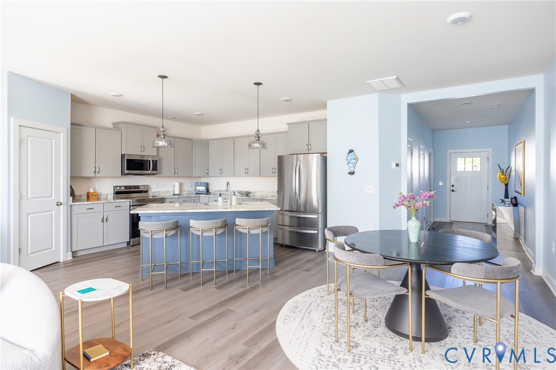 Kitchen featuring a central island with a stone countertop, grey shaker-style cabinetry, stainless steel appliances, dual pendant lighting, and wood-finish flooring Kitchen featuring a central island with a stone countertop, grey shaker-style cabinetry, stainless steel appliances, dual pendant lighting, and wood-finish flooring