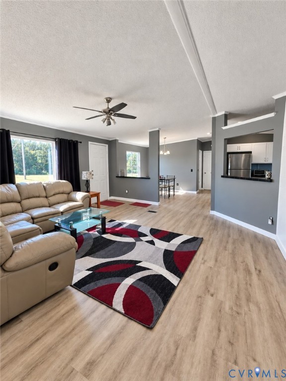 Living area featuring wood-finish flooring, neutral grey wall paint, a ceiling-mounted fan, and a pass-through opening to the kitchen Living area featuring wood-finish flooring, neutral grey wall paint, a ceiling-mounted fan, and a pass-through opening to the kitchen