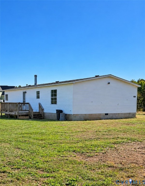 Exterior featuring white vinyl siding, a raised wood deck with integrated stairs, and a concrete block foundation set on a expansive grass lot Exterior featuring white vinyl siding, a raised wood deck with integrated stairs, and a concrete block foundation set on a expansive grass lot