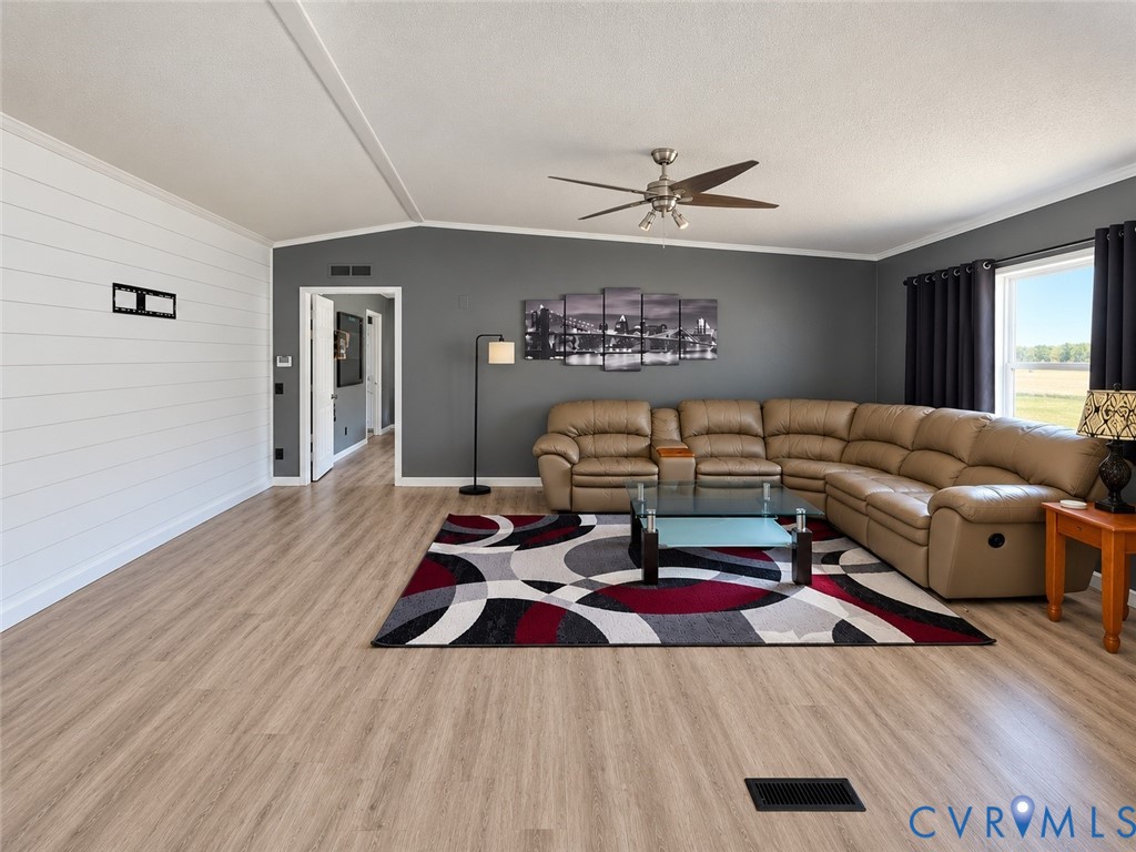 Living area featuring wood-finish flooring, white shiplap accent wall, grey wall paint, and a ceiling-mounted fan with integrated lighting Living area featuring wood-finish flooring, white shiplap accent wall, grey wall paint, and a ceiling-mounted fan with integrated lighting