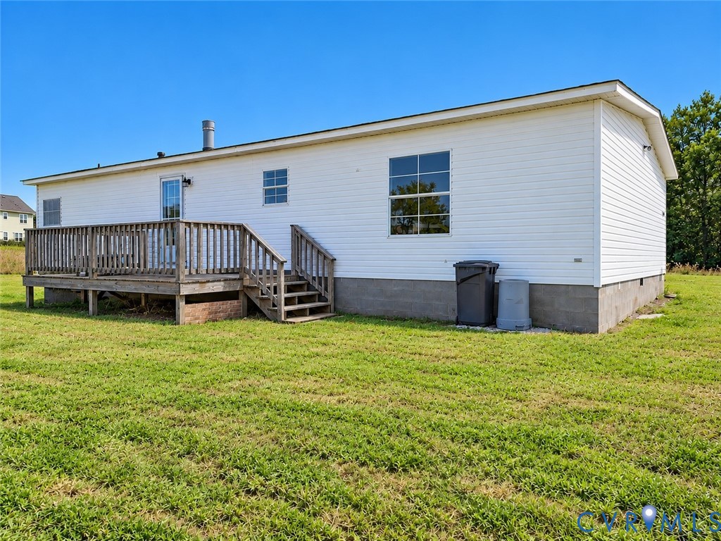 Exterior featuring white horizontal siding, a raised wood deck with staircase, and a concrete block foundation set on an expansive grass lot Exterior featuring white horizontal siding, a raised wood deck with staircase, and a concrete block foundation set on an expansive grass lot