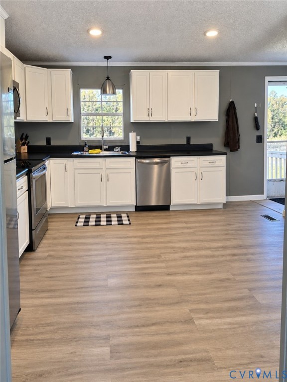 Kitchen featuring white shaker-style cabinetry, contrasting dark countertops, stainless steel appliances, a single-basin sink with a pendant light fixture, and wood-finish flooring