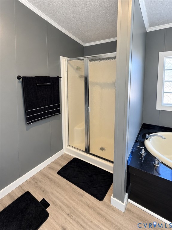 Standalone shower with a glass-paneled door, soaking tub with a dark surround, and wood-finish flooring