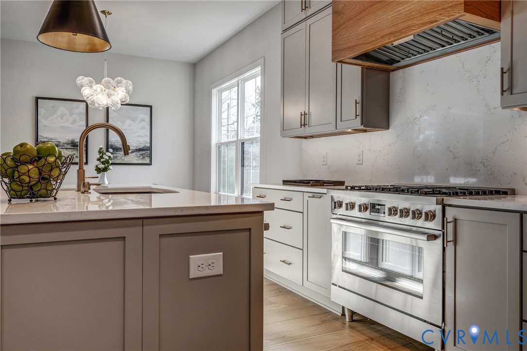 Kitchen featuring shaker-style cabinetry, a quartz countertop, a stainless steel gas range, a wood-finish vent hood, and wood-finish flooring Kitchen featuring shaker-style cabinetry, a quartz countertop, a stainless steel gas range, a wood-finish vent hood, and wood-finish flooring