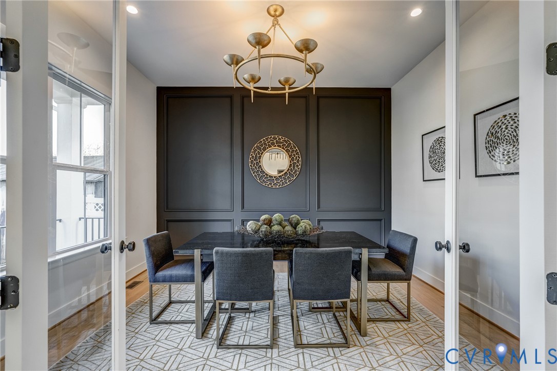 Interior room featuring dual glass-panel entry doors, a dark-toned accent wall with custom picture-frame molding, and a tiered brass chandelier Interior room featuring dual glass-panel entry doors, a dark-toned accent wall with custom picture-frame molding, and a tiered brass chandelier