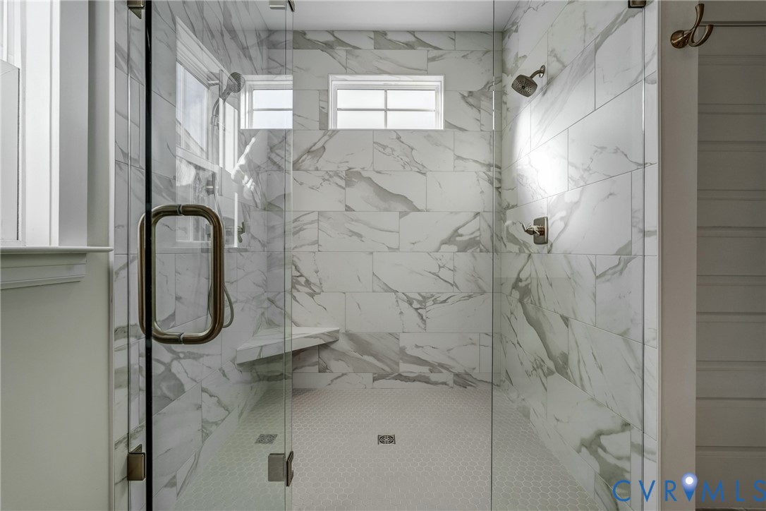 Walk-in shower featuring large-format stone-patterned wall tile, frameless glass enclosure, built-in corner bench, and dual wall-mounted shower heads Walk-in shower featuring large-format stone-patterned wall tile, frameless glass enclosure, built-in corner bench, and dual wall-mounted shower heads