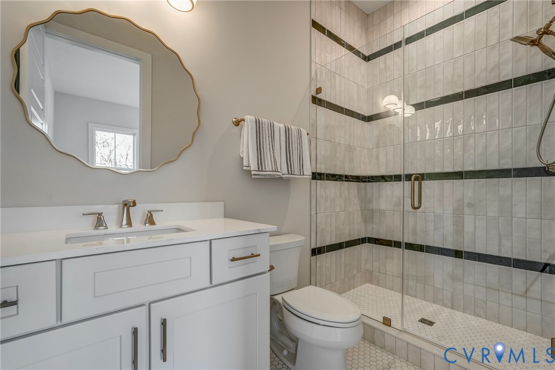 Bathroom featuring a white vanity with a solid-surface countertop, an oval wall mirror with scalloped gold-tone trim, a walk-in shower with a glass enclosure, and decorative tile accents Bathroom featuring a white vanity with a solid-surface countertop, an oval wall mirror with scalloped gold-tone trim, a walk-in shower with a glass enclosure, and decorative tile accents