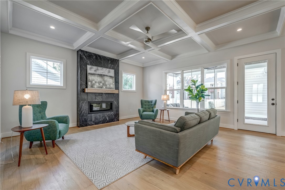 Coffered ceiling, full-height dark stone fireplace surround, light-toned wood-finish flooring, and recessed lighting Coffered ceiling, full-height dark stone fireplace surround, light-toned wood-finish flooring, and recessed lighting