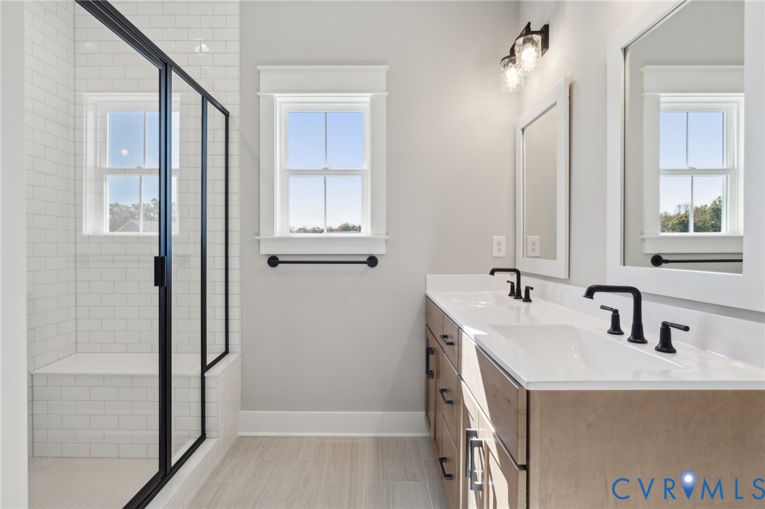 Double vanity with stone countertop and matte black fixtures, walk-in shower with white subway tile, built-in shower bench, and wood-finish cabinetry