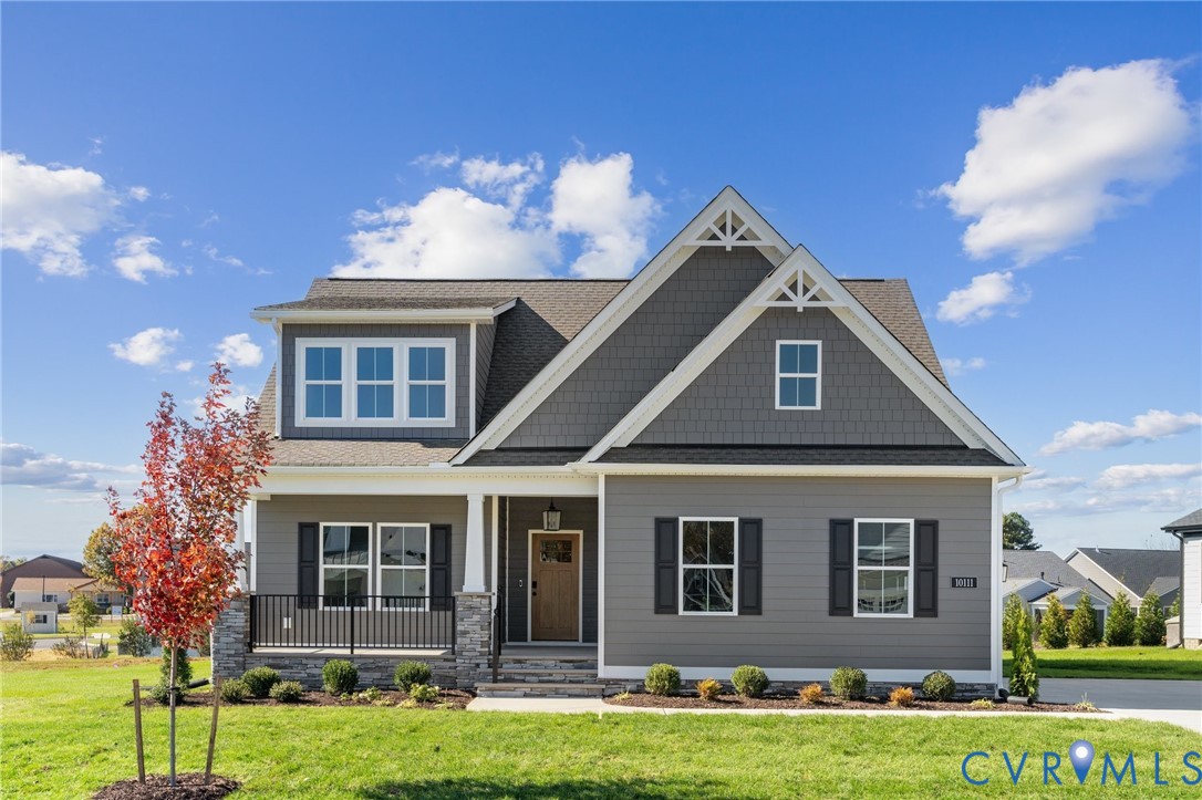 Two-story residence featuring horizontal and shingle-style siding, a covered front porch with stone-veneer accents, gable roof detailing, and dark-framed shutters
