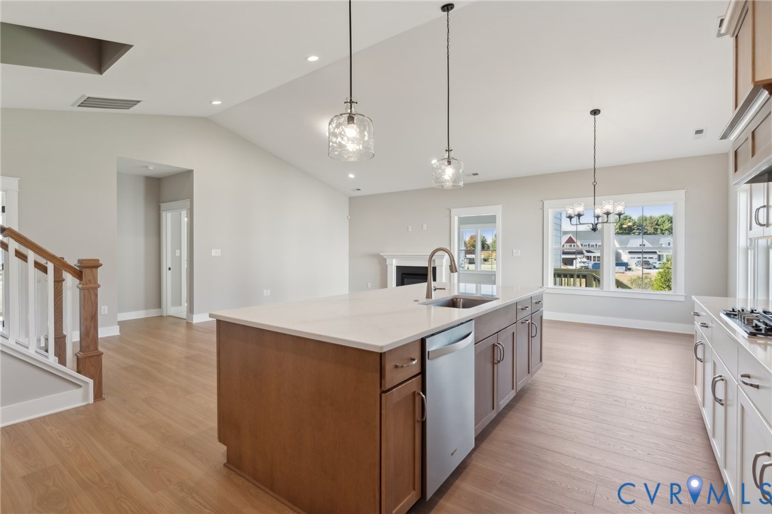 Kitchen featuring a center island with a stone-finish countertop, stainless steel dishwasher, vaulted ceiling, wood-finish flooring, and pendant lighting