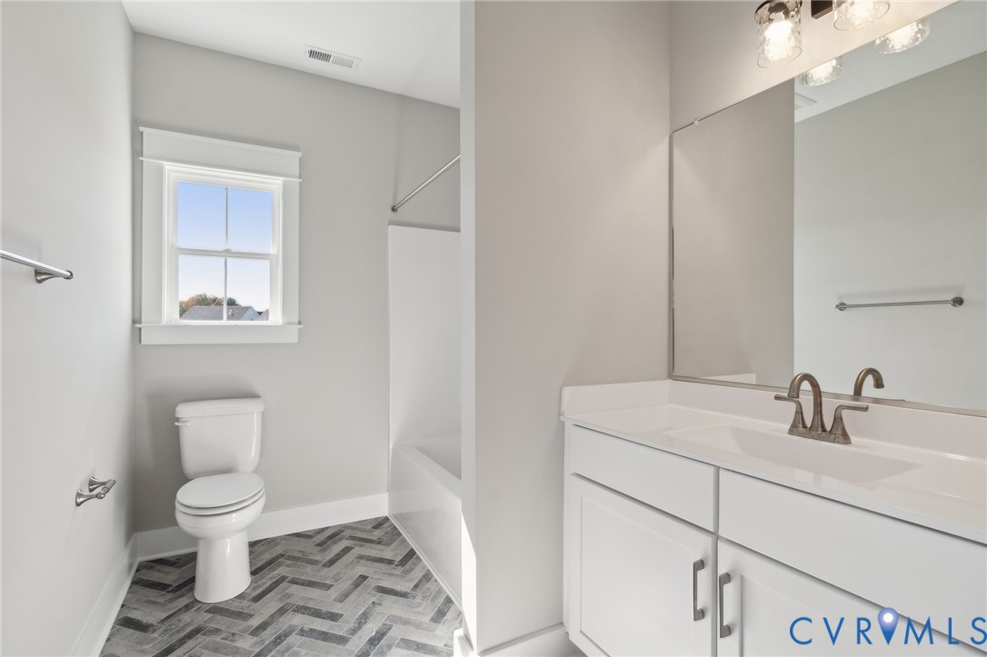 Bathroom featuring white cabinetry, an integrated vanity top, multi-light fixture, herringbone-patterned flooring, and a window with casing trim
